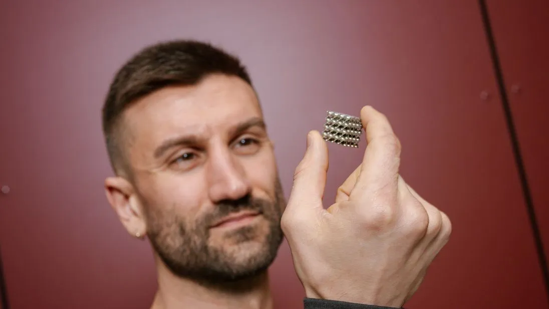 Ein Mann hält einen Würfel aus Metall in der Hand.